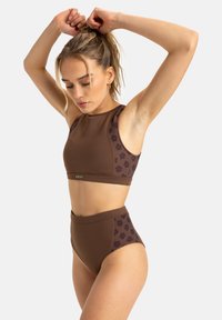 Braunes Sportoutfit bestehend aus einem croppeden Top und hoch tailliertenBottoms, mit floralen Mustern und einem Logo-Highlight am Bund.