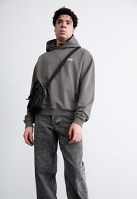 Grå sweatshirt med frontlomme, parret med grå denimjeans. Modellen bærer en sort crossbody taske med flere lynlåslommer.