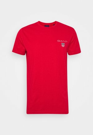 T-shirt en coton rouge avec col rond, manches courtes et un petit logo brodé sur le côté gauche de la poitrine avec un design en forme de bouclier.