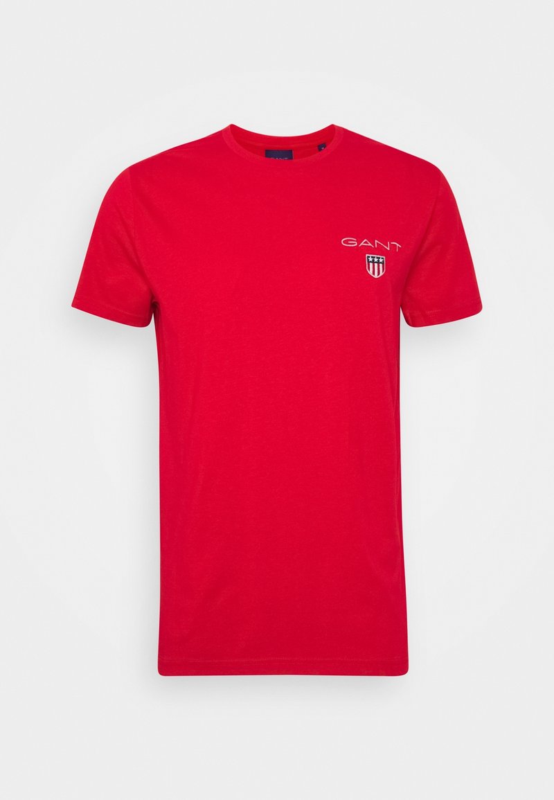 T-shirt en coton rouge avec col rond, manches courtes et un petit logo brodé sur le côté gauche de la poitrine avec un design en forme de bouclier.