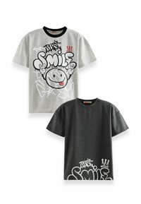 Kaksi graafista t-paitaa; yksi harmaa mustalla kauluksella, suuri "Just Smile" -kuvio, ja yksi tumma harmaa valkoisilla yksityiskohdilla ja samankaltaisella kuviolla.