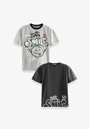 To grafiske t-shirts; en grå med sort krave, stor "Just Smile" design, og en mørkegrå med hvide accenter og lignende design.