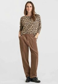 Top de manga larga con estampado de leopardo en beige y marrón, combinado con pantalones anchos de pierna ancha texturizados en marrón. Modelo de pie con las manos en los bolsillos.