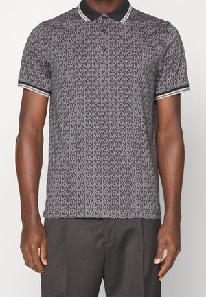 Homme portant un polo gris à manches courtes avec un motif MK intégral, col noir et poignets noirs avec des bandes blanches, associé à un pantalon gris.