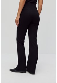 Zwarte flared broek van soepele stretchstof, met een hoge taille en twee achterzakken, gecombineerd met puntige zwarte schoenen.
