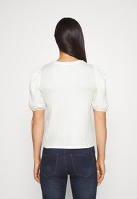 Top blanco texturizado con mangas abullonadas, cuello redondo y un corte corto, combinado con jeans azul oscuro que cuentan con dos bolsillos traseros.