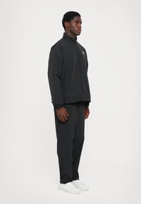 Black zip-up jacket with elastic cuffs, paired with matching pants. Features a simple design and is made from lightweight material. White sneakers.