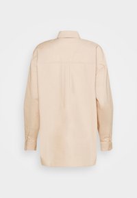Camicia beige a maniche lunghe con colletto e polsini abbottonati. Presenta una piega centrale sul retro e un orlo diritto. Tessuto dalla texture liscia.