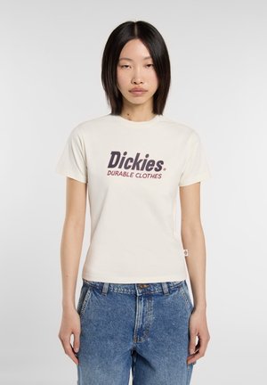 Crème katoenen T-shirt met een voorzijdeafbeelding met "Dickies" en "DUURZAME KLEDING" in donkerrood, gecombineerd met hoge blauwe spijkerbroek.