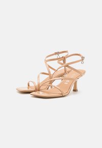Sandali con cinturini nude in patent, con punta affilata, sottili cinturini alla caviglia e tacco a blocco di 5 cm; texture liscia e design minimalista.