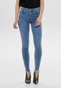 Blue skinny jeans with a high waist, featuring a five-pocket design and subtle whiskering, paired with black high-heeled shoes.