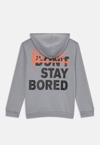 Haut à capuche gris avec une capuche, présentant un impressionnante impression texte en noir disant "NE RESTEZ PAS ENNUYÉ," et un "TOUJOURS" en style graffiti orange au-dessus.