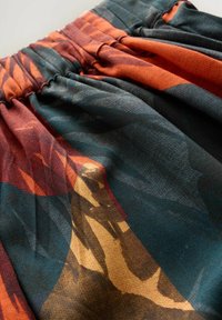 Gemusterter Stoff in den Farbtönen Teal, Orange und Braun, mit einem gerafften Taillenbund und einer weichen, strukturierten Oberfläche.