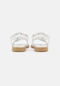 Białe sandały z kwiecistym wzorem na paskach, przezroczystymi sekcjam i beżowymi gumowymi podeszwami. Posiadają regulowane paski dla lepszego dopasowania.