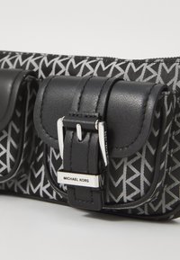 Sac noir et argent avec un motif géométrique, deux fermetures à boucle en cuir et une plaque en métal avec le logo "MICHAEL KORS."