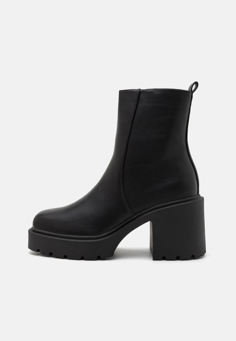 Botines de cuero negro hasta el tobillo con un tacón grueso, textura suave, suela de zigzag y una lengüeta en el talón para facilitar su uso.