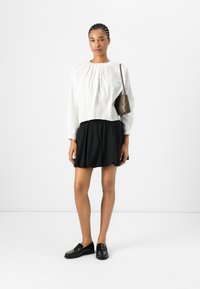 Hvit plisserte langtærmet bluse, svart elastisk midje mini skjørt, svarte loafers og en liten brun crossbody veske. Enkelt, moderne design.