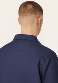 Navyblauwe shirt van een gestructureerde stof, met een klassieke kraag en zichtbare stikseldetails langs de schouders en de rug.