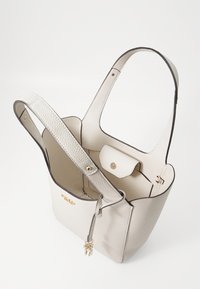 Sac fourre-tout en cuir couleur crème avec une finition texturée, ouverture sur le dessus et deux anses, présentant des ferrures dorées et une poche intérieure.