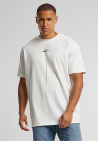 Camiseta de algodón blanca con cuello redondo y mangas cortas. En la parte frontal presenta un gráfico de texto negro que dice "PIENSA DIFERENTE."