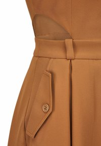 Detail van een bruine jurk met een stoffen riem die in de taille is gestrikt en een klepzak aan de zijkant met knoop.