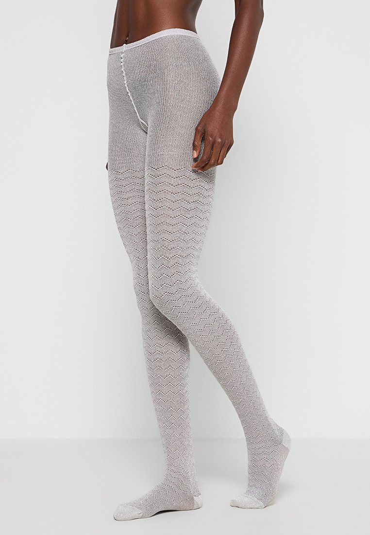 Szare dzianinowe legginsy z falistym wzorem, z wysokim stanem i miękką teksturą. Skarpetki mają jednolitą szarość na dole.
