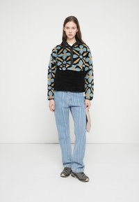 Fuzzy black and colorful patterned fleece pullover with a half-zip and collar, paired with light blue striped jeans and dark sneakers.