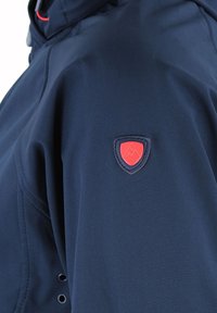 Chaqueta softshell en color marino con capucha con cremallera, que presenta un emblema rojo y azul en la manga y un tejido texturizado para mayor comodidad y durabilidad.