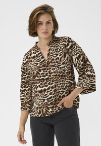 Blouse met luipaardprint en V-hals, driekwart mouwen en een relaxte pasvorm; kleuren zijn beige, bruin en zwart. G gedragen met donkere jeans.