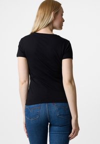 Czarna koszulka z krótkim rękawem i okrągłym dekoltem, wykonana z miękkiej bawełny, noszona z niebieskimi dżinsami z kontrastowym przeszyciem i tylnymi kieszeniami.