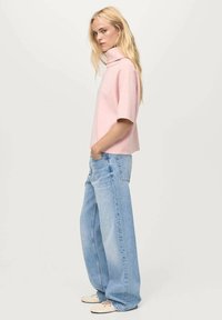 Maglione rosa a maniche corte con colletto alto, abbinato a jeans a gamba larga blu chiaro. L'outfit presenta una vestibilità rilassata e un design semplice.