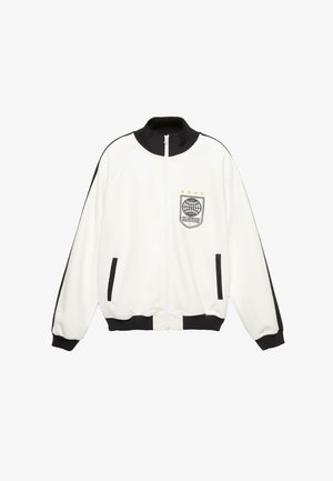 Biała kurtka na zamek z czarnym kołnierzem, mankietami i wykończeniem kieszeni; czarne paski na rękawach; naszywka z globusem i gwiazdami na piersi.