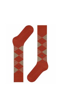 Calzini con motivo argyle in tonalità caldo rosso, beige e rosa chiaro, mostrati con un calzino disteso e l'altro in posizione verticale per mostrare il design.