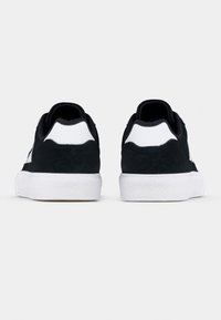 Black suede sneakers with white accents, rounded shape, flat rubber sole, padded collar, and textured back panel.