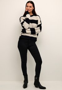 Maglione a maglia grossa con righe orizzontali navy e crema, dal fit rilassato e maniche lunghe. Abbinato a jeans neri attillati e stivali alla caviglia.