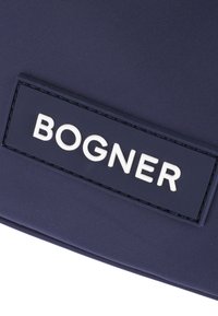 Marineblå tekstilpose med et rektangulært mærke med præget hvide bogstaver, der staver "BOGNER." Overfladen har en struktureret finish.