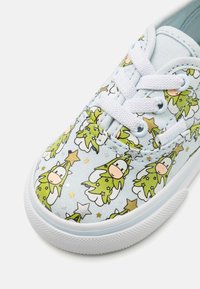 Light blue canvas sneaker featuring a playful pattern of green figures with stars and subtle details, white laces, and textured rubber sole.
