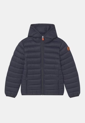 Chaqueta acolchada con capucha en azul marino, con pespuntes horizontales, cremallera frontal, puños elásticos y un pequeño parche redondo con logo en la manga izquierda.