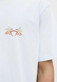 Lichtblauw katoenen t-shirt met een klein geborduurd ontwerp van bladeren en een lint met tekst, gepositioneerd op de borst.