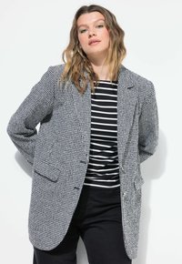 Černobílý houndstooth blazer se strukturovaným střihem, obsahující dvě přední kapsy a knoflíky ve zlatém tónu, nošený přes černobílou pruhovanou košili.