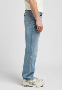 Ljusblå raka jeans med fem fickor, subtil sömnad och en urtvättad finish, i kombination med beigea träningsskor.