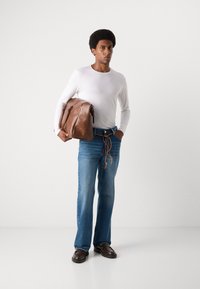 Braune Leder-Umhängetasche, weißes Langarmhemd, hellblaue Schlagjeans, braune Schuhe. Einfaches Design mit lässigem Look und natürlichen Texturen.