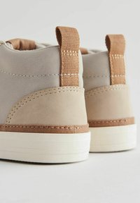 Bottines grises et beiges avec une texture lisse, accents marron contrastants, semelles en caoutchouc et languettes en tissu à l'arrière.