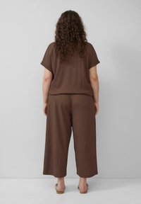 Bruine, kortärmige top en wijde broek van textuurstof. Eenvoudig ontwerp met een ontspannen pasvorm. Schoeisel bestaat uit minimale bruine sandalen.