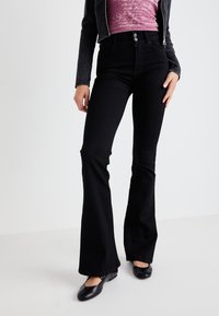 Black flared jeans with a high waistband and two-button closure. Smooth denim texture, fitted through the hips, flaring at the knees.
