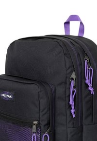 Czarny plecak z fioletowymi akcentami, wyposażony w główną komorę, przednią siatkową kieszeń, wytrzymałą tkaninę oraz podwójne zamki błyskawiczne z uchwytami.