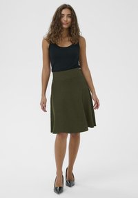 Gonna a campana verde oliva in un tessuto testurizzato con vita alta, abbinata a un top senza maniche nero e a décolleté neri con punta.