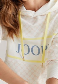 White hoodie with pink geometric pattern, yellow drawstrings, and blue "JOOP!" text. Features ribbed cuffs and hem for added texture.