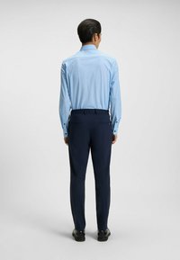 Camicia azzurro chiaro con piccoli pois blu scuro, abbinata a pantaloni blu scuro e scarpe nere. La camicia presenta un colletto a punta.