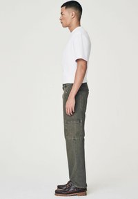Pantaloni cargo de culoare verde măslin, cu o croială dreaptă, buzunare laterale și cusături contrastante, asortați cu un tricou alb și pantofi negri.